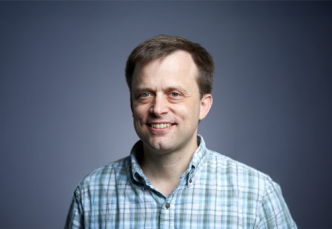 A color photo of Andrew Myers in front of a grey background