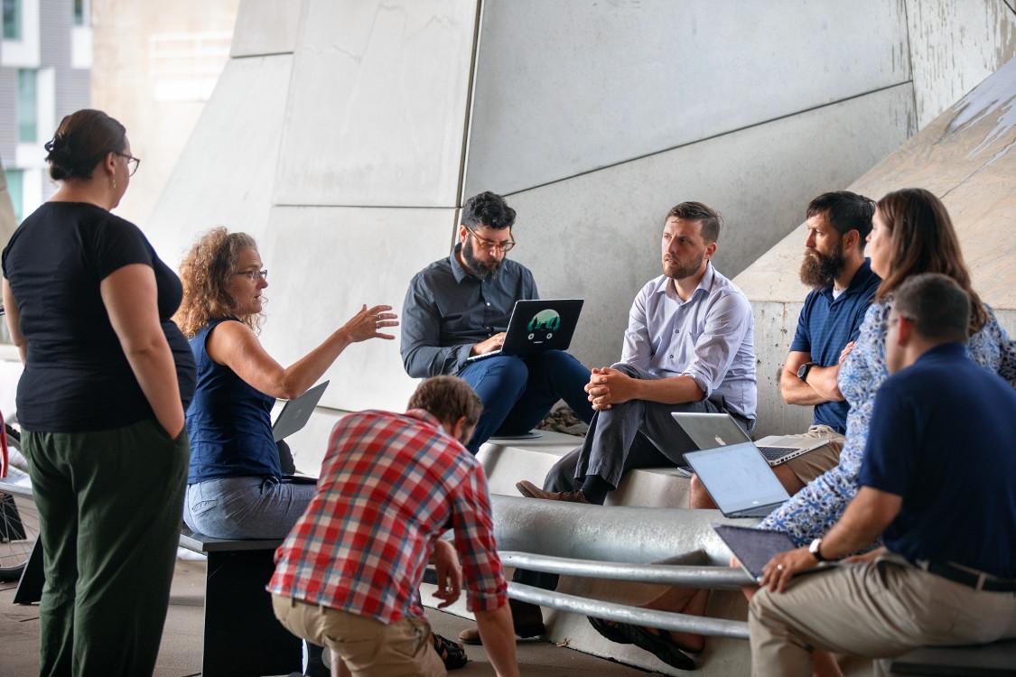 woman in blue shirts talks with a group of people seated around her
