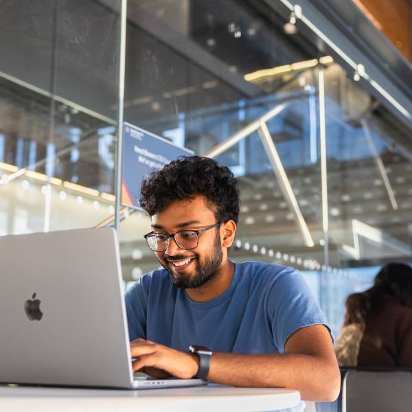 A color photo of a man smiling working on a laptop