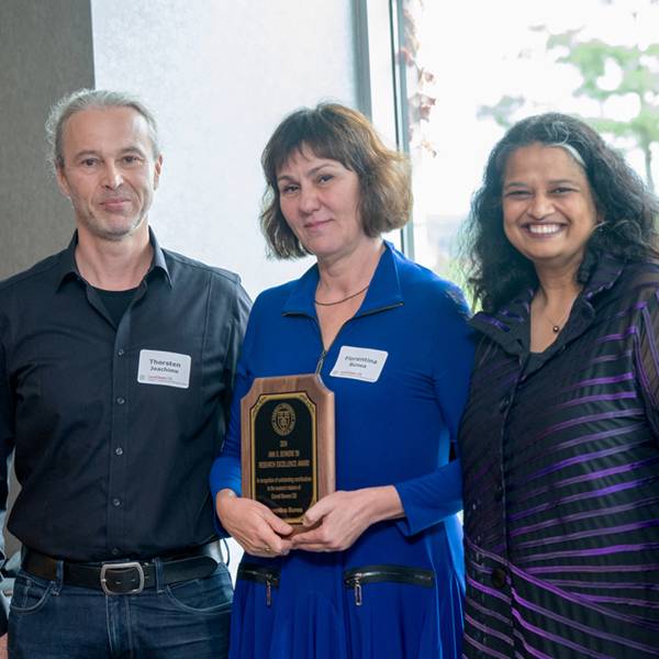 A color photo showing a man and two women posing for a photo. The woman in the middle is holding an award