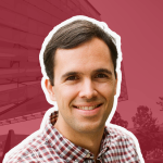 A color photo of a man smiling for a photo with a red background