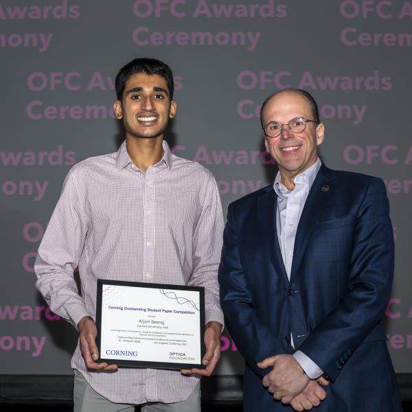 A color photo of two men. One holding a certificate.